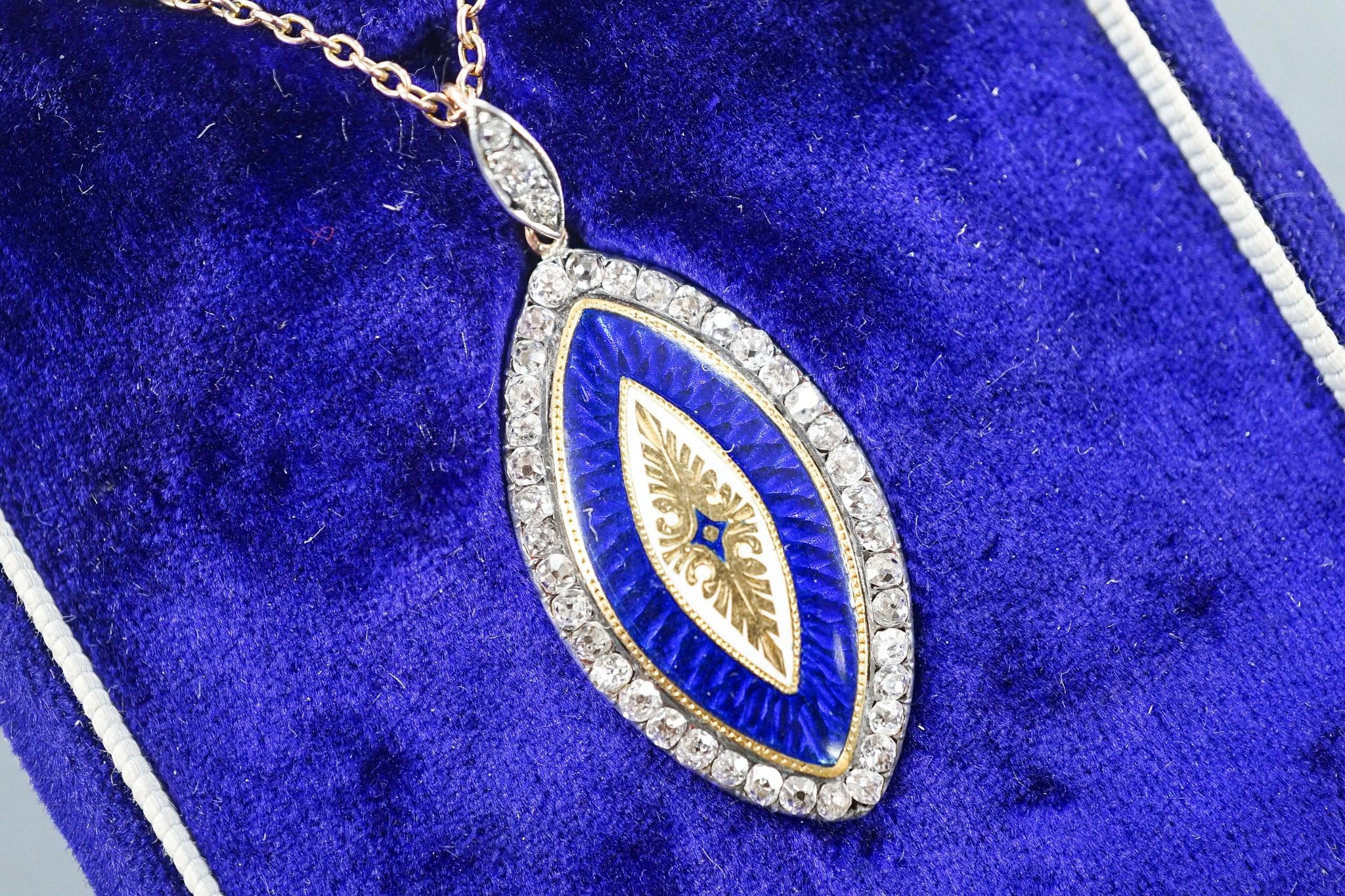 An early 20th century yellow metal, two colour enamel and diamond set navette shaped pendant, 32mm, on a yellow metal chain, 47cm, gross weight 6.9 grams.